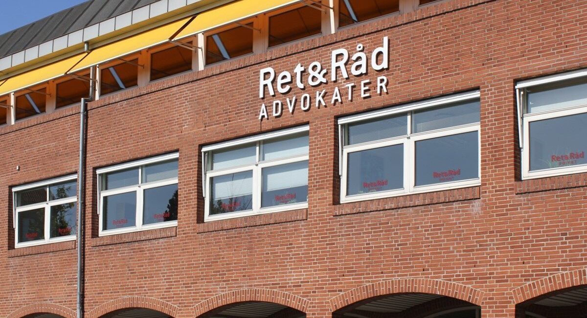 Bygning med rød murstensfacade, vinduer og skiltet "Ret&Råd Advokater".